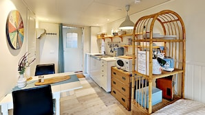 A compact kitchen with a dining area, featuring a wooden cabinet with a hanging rack, a microwave, and a sink. - Woodstock B&B & Studio Apartments (Balsta)