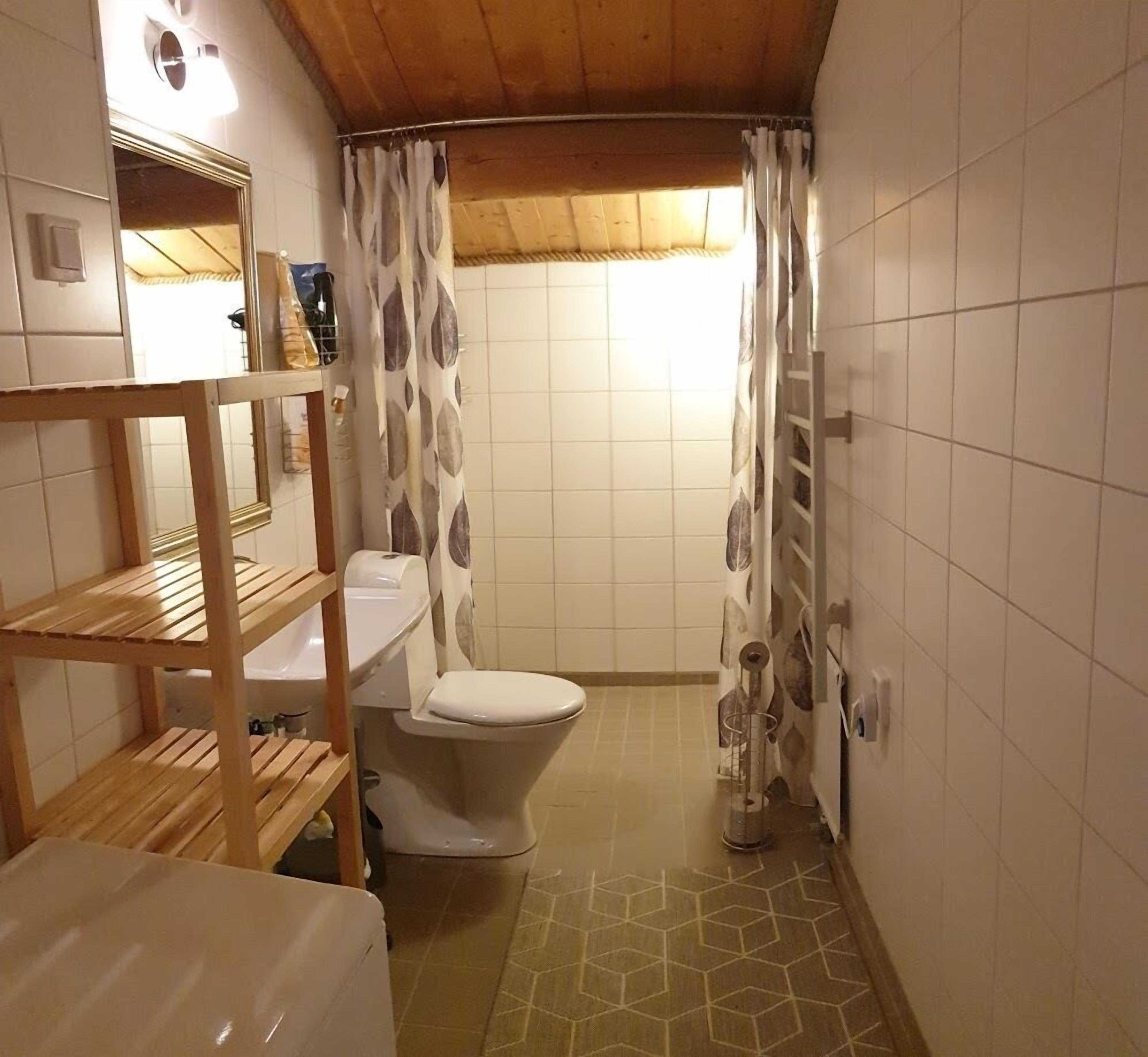 Un bagno piccolo ma funzionale, con il water, una mensola in legno, uno specchio e una tenda da doccia con un motivo a foglie.