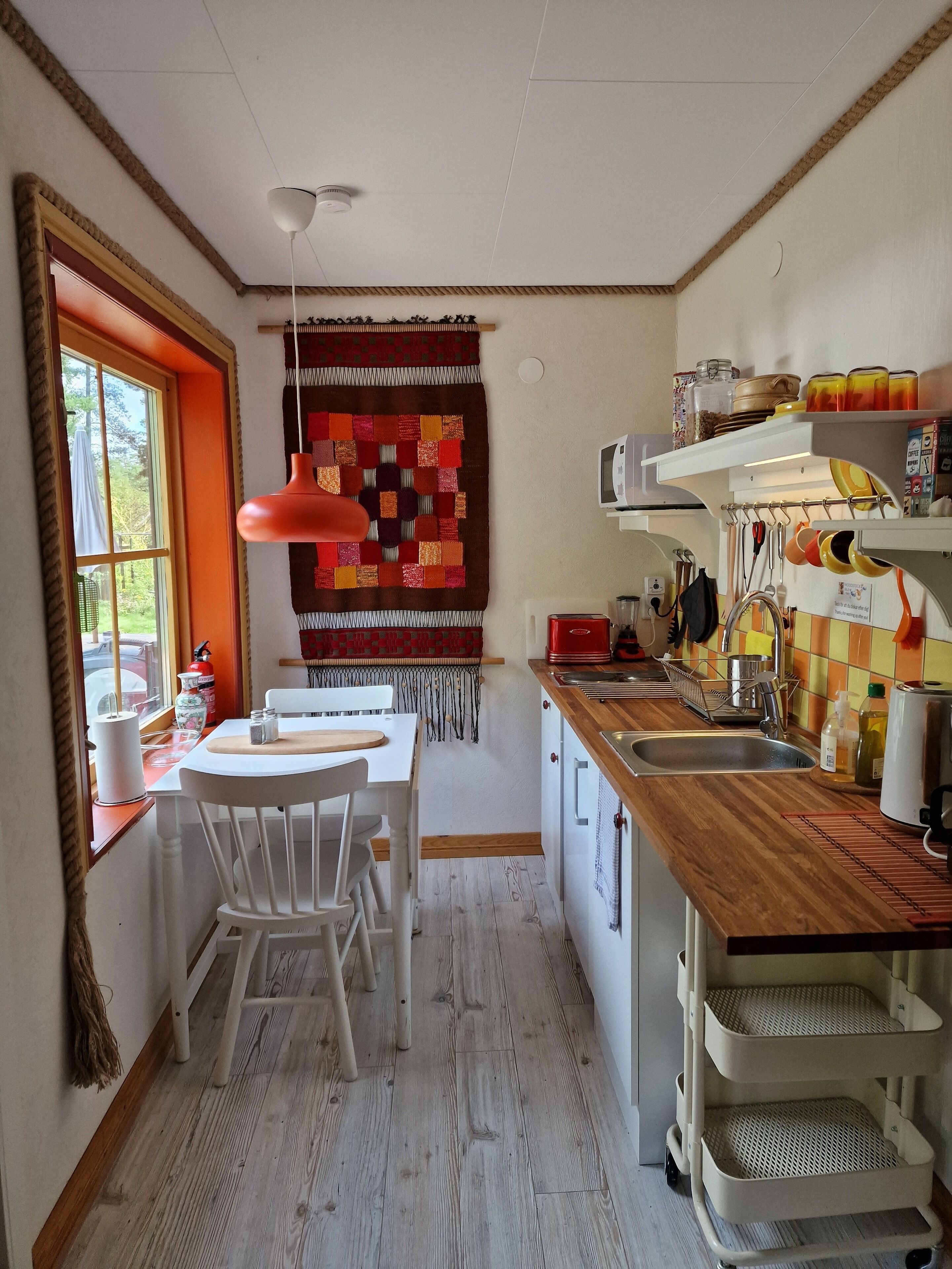 A compact kitchen with a dining area, featuring a wooden countertop, white cabinets, and a hanging light fixture.