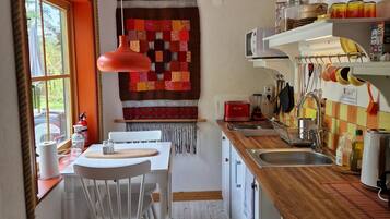 A compact kitchen with a dining area, featuring a wooden countertop, white cabinets, and a hanging light fixture.
