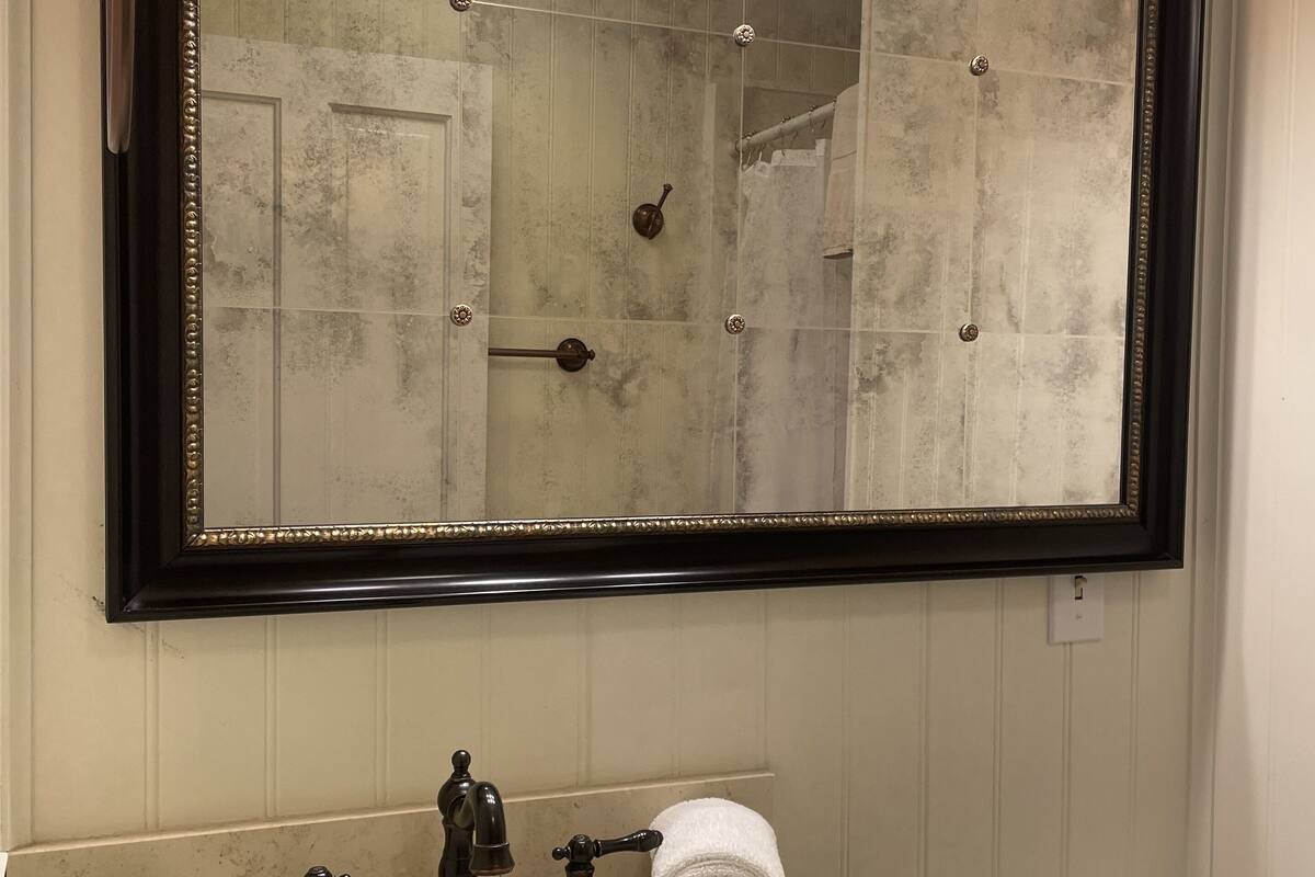 Un baño con un espejo grande, tres luces empotradas en la pared, un lavabo con dos grifos y un inodoro.