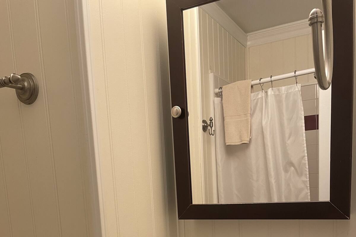 Un baño con lavamanos, espejo, toallero y dispensador de papel higiénico.