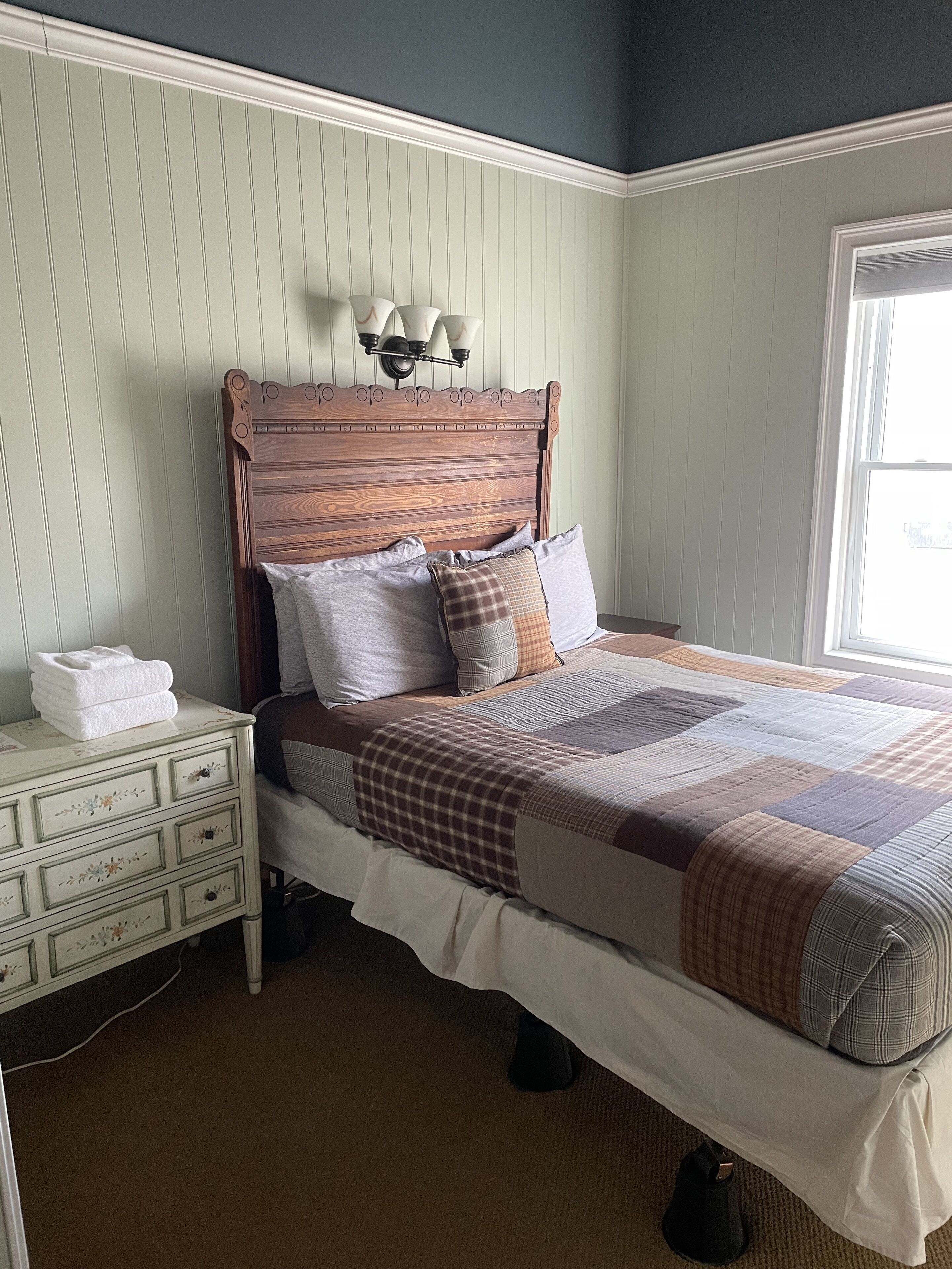A bedroom with a wooden headboard, a quilted bedspread, and a nightstand with a lamp.