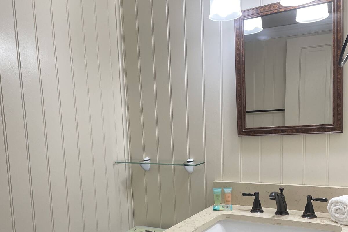 Un baño con inodoro blanco, tocador de madera con lavabo y espejo sobre el tocador.