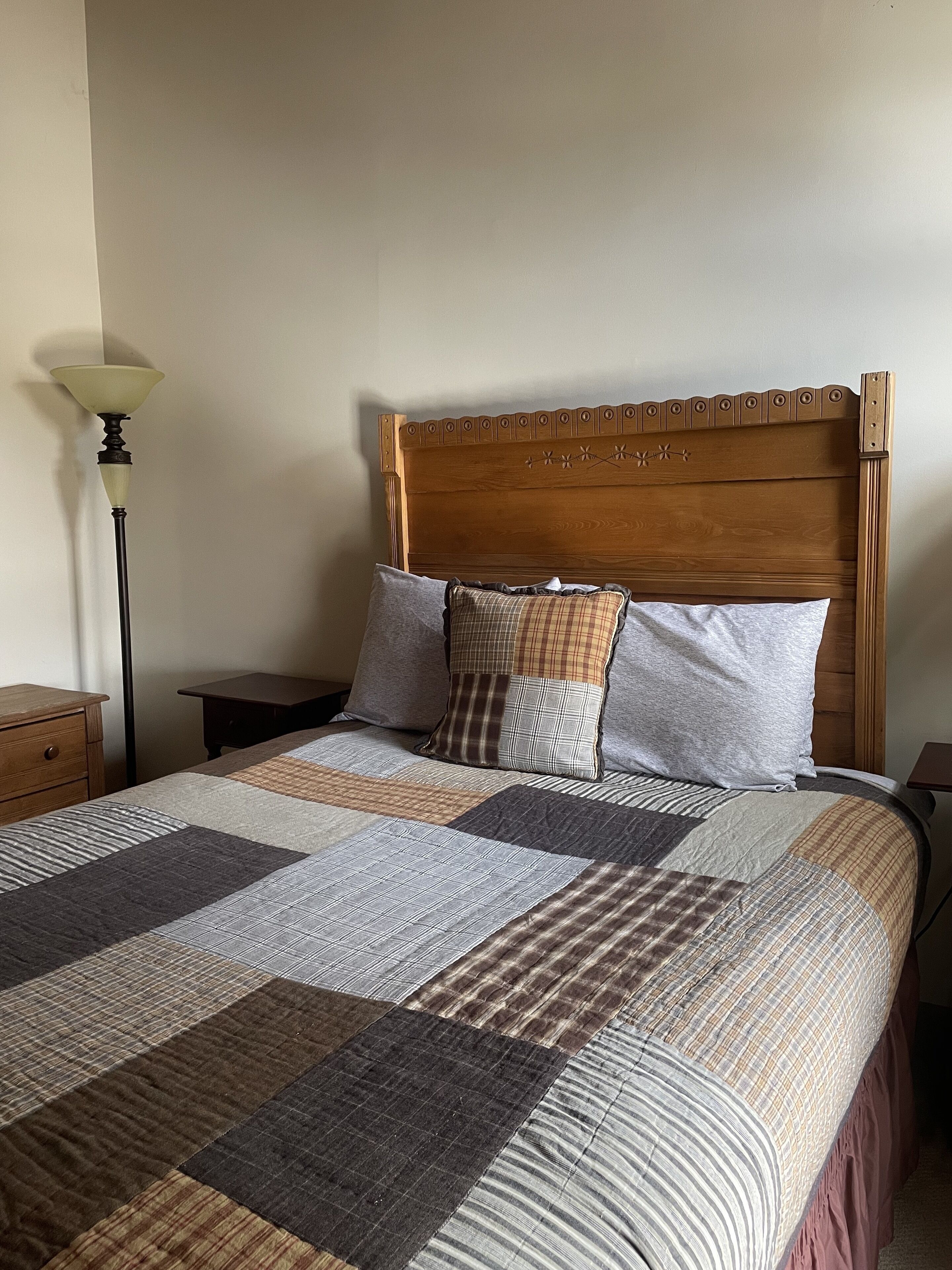 A neatly made bed with a wooden headboard, a quilt with various patterns, and two bedside tables with lamps.