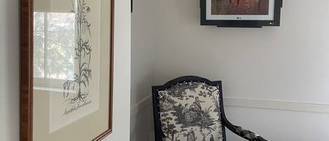 Une pièce décorée d’une estampe botanique encadrée, d’une œuvre d’art encadrée et d’un fauteuil à motifs à carreaux.