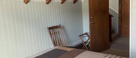 A room with a sloped ceiling, a bed with a quilt, a wooden chair, and a door leading to another room.