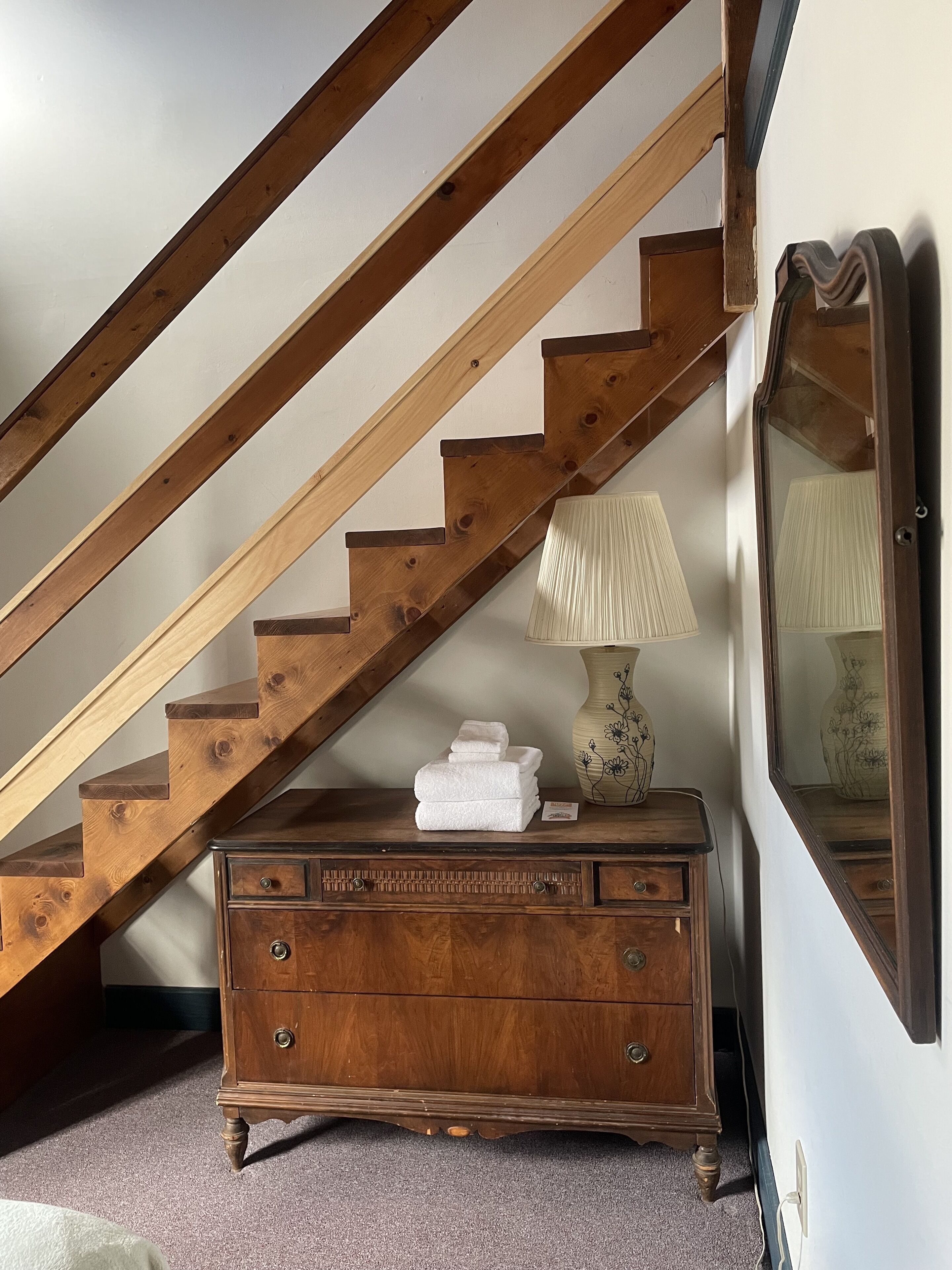 A wooden staircase with a lamp and a dresser in a room.