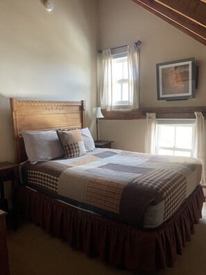 A neatly made bed with a wooden headboard, a window with curtains, and a framed picture on the wall. - The Waitsfield Inn (Waitsfield)