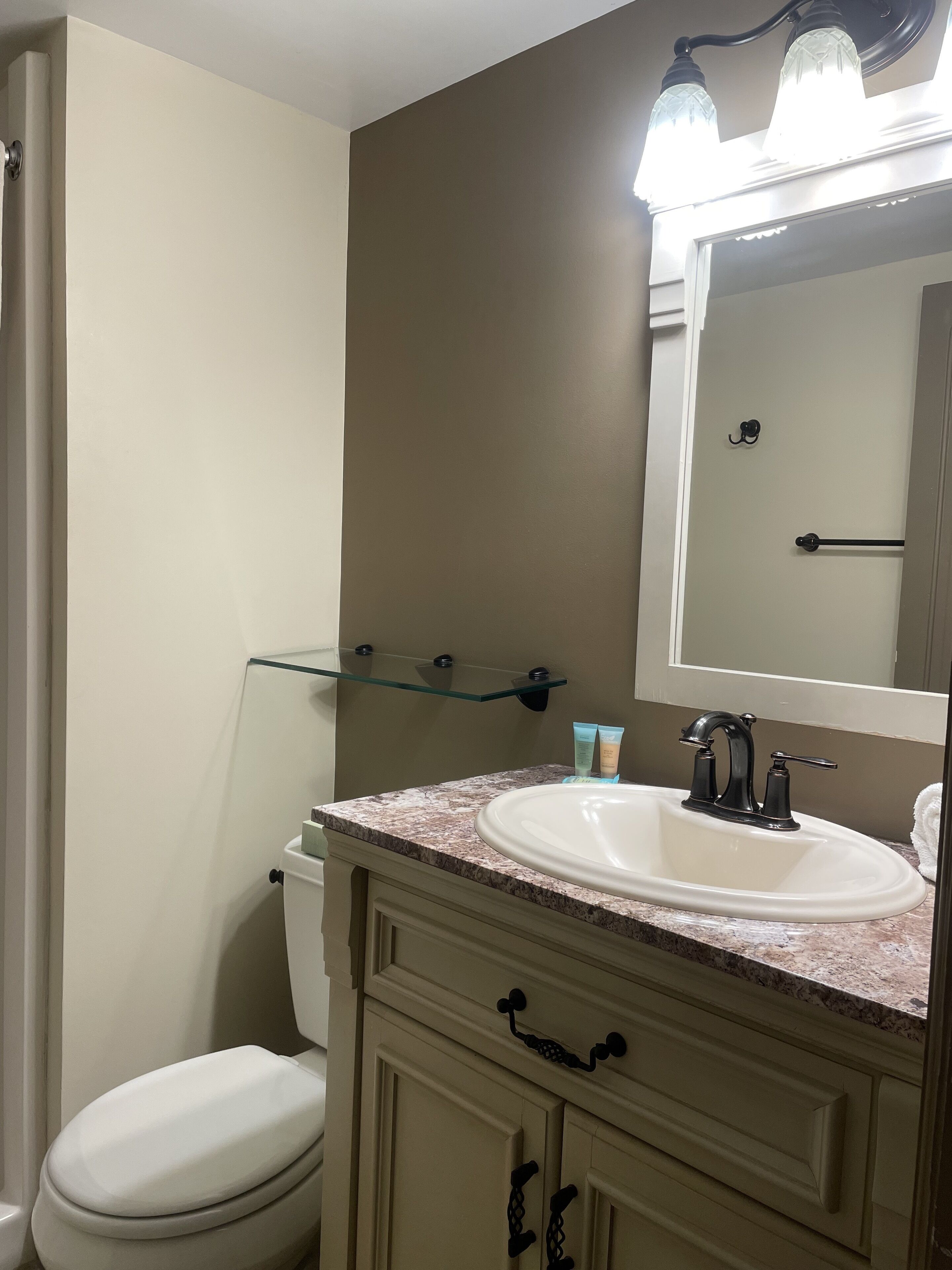 Une salle de bain avec des toilettes blanches, un lavabo beige doté d’un robinet noir, et un miroir au-dessus du lavabo.