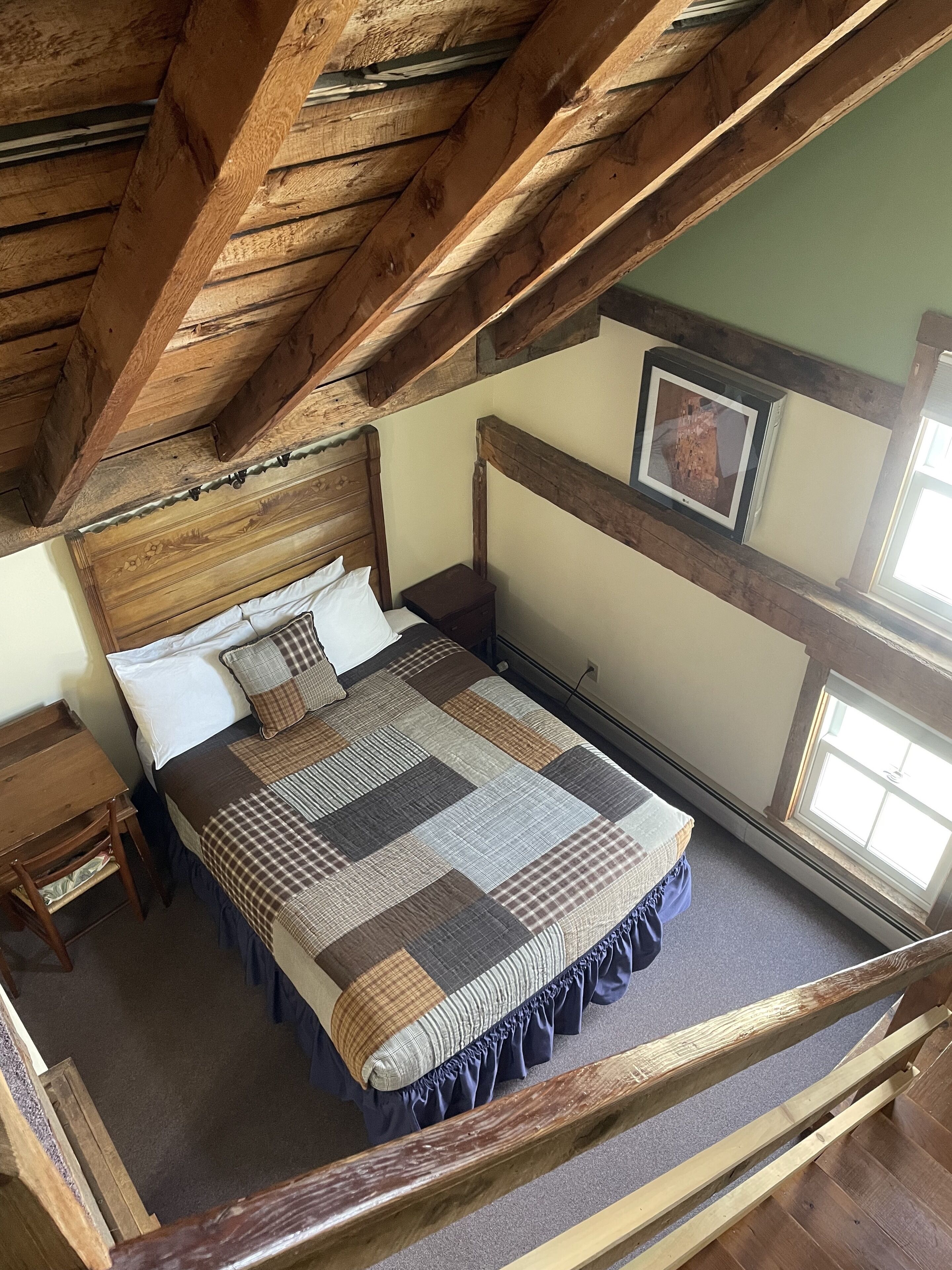 Une chambre avec un plafond en bois, un lit recouvert d’une courtepointe, une table de chevet et un tableau encadré accroché au mur.