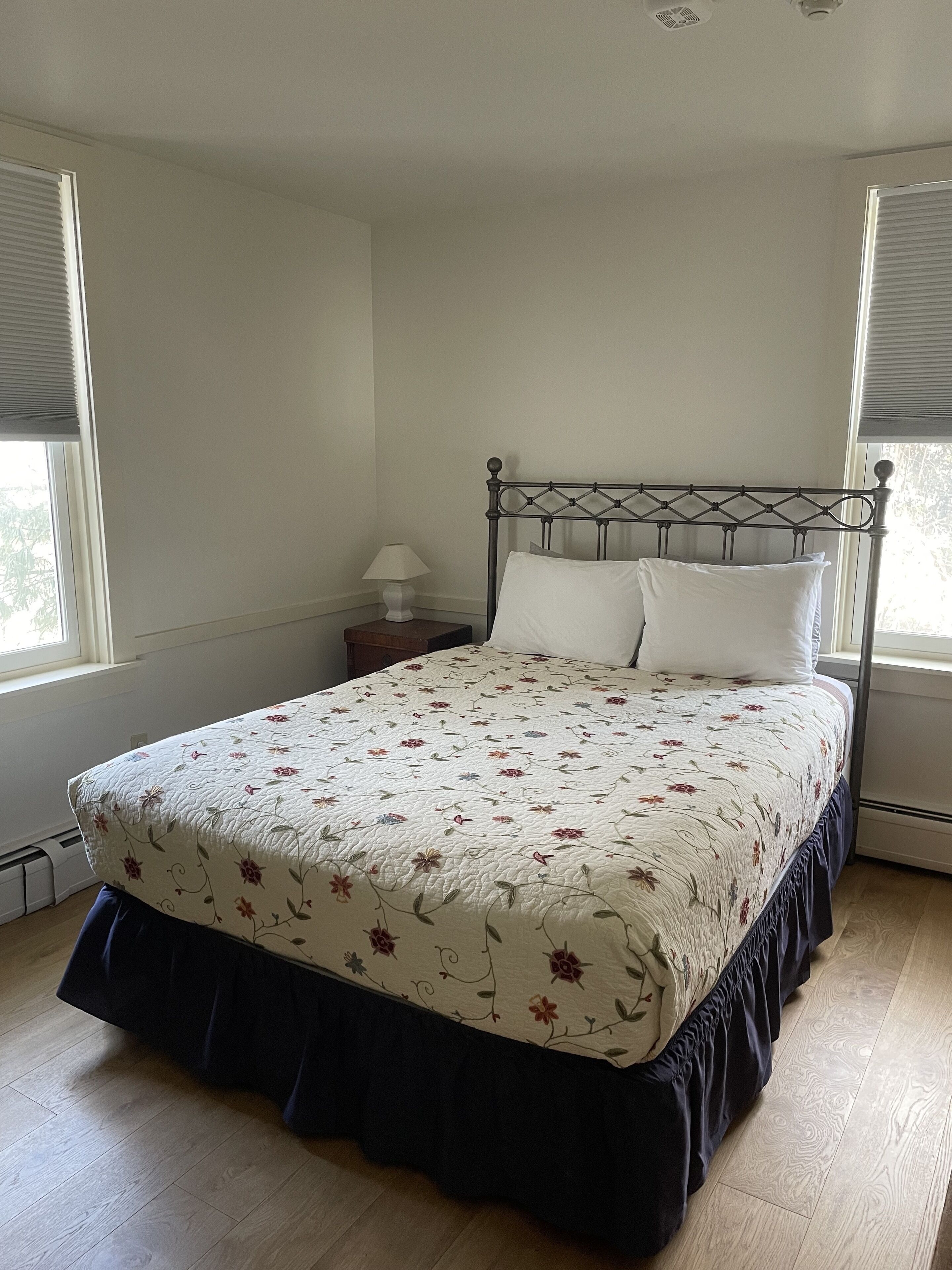 A bedroom with a bed, a nightstand, a lamp, and a window with blinds.
