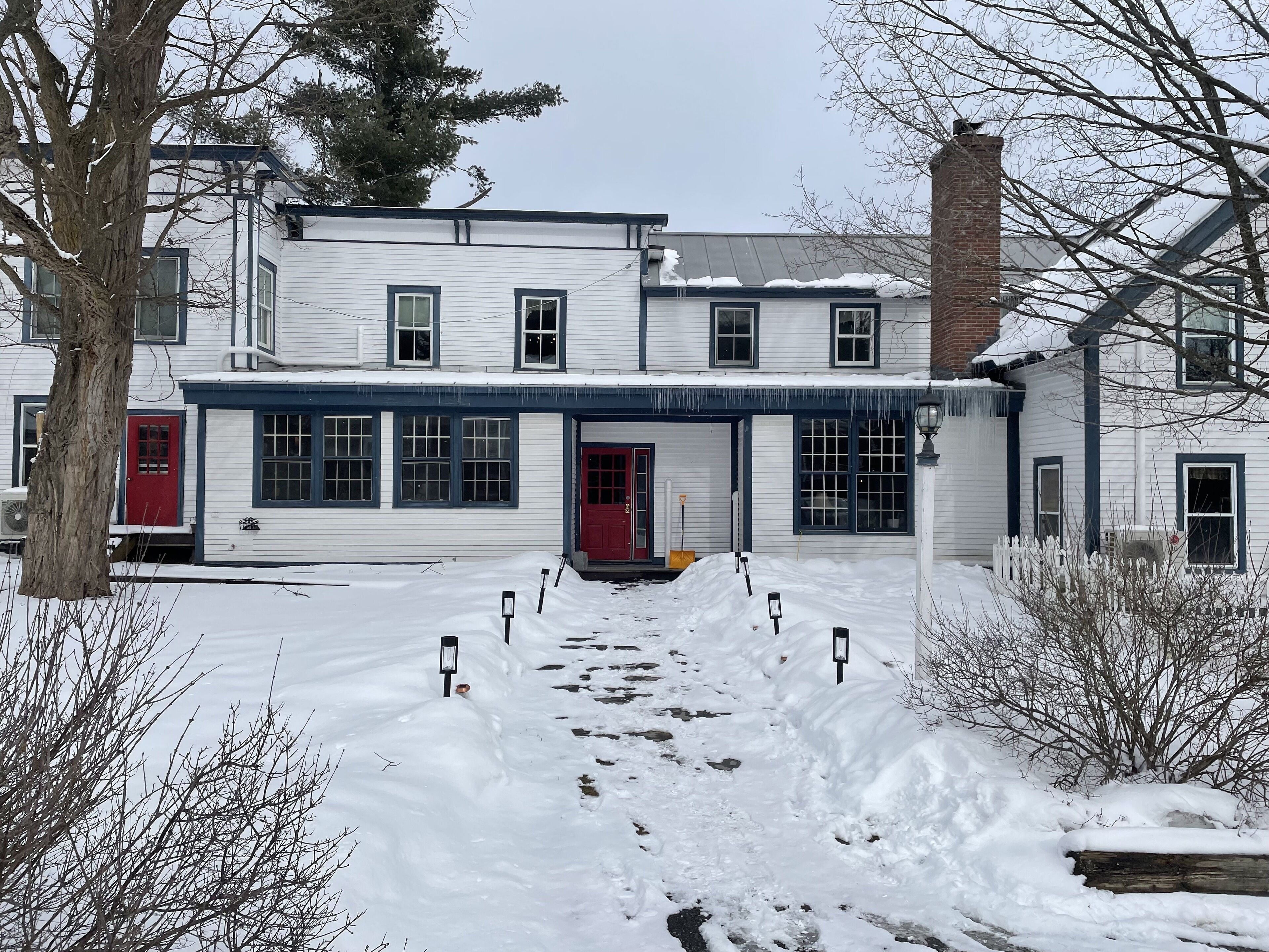 A two-story house with a red door and multiple windows, surrounded by snow.