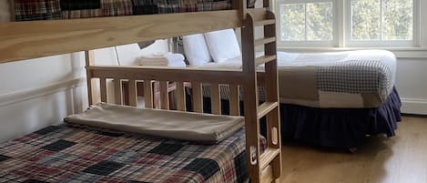 A bunk bed with a plaid quilt, a wooden ladder, and a window with blinds.