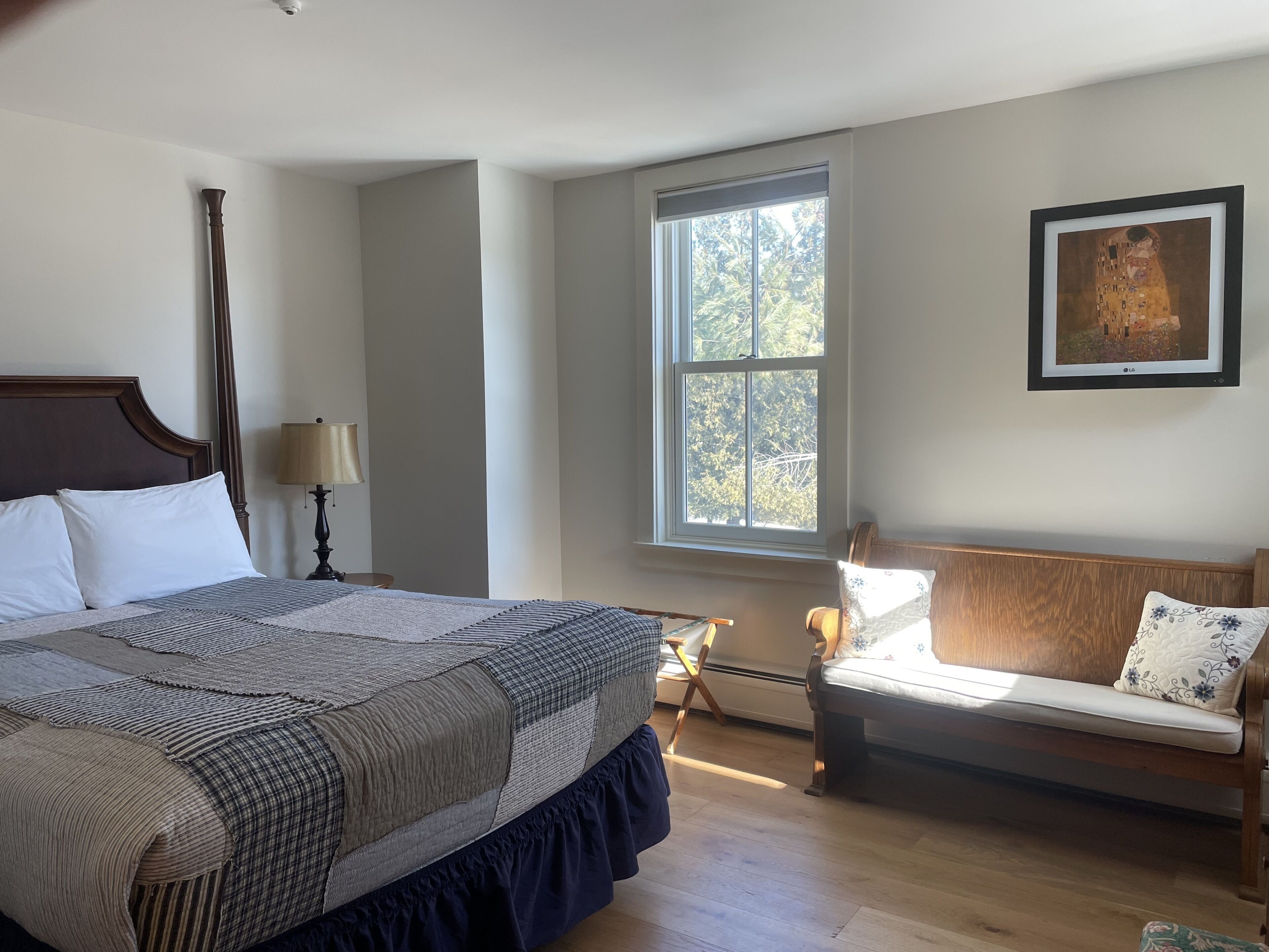 Un dormitorio con una cama grande, un banco, una ventana y un cuadro en la pared.