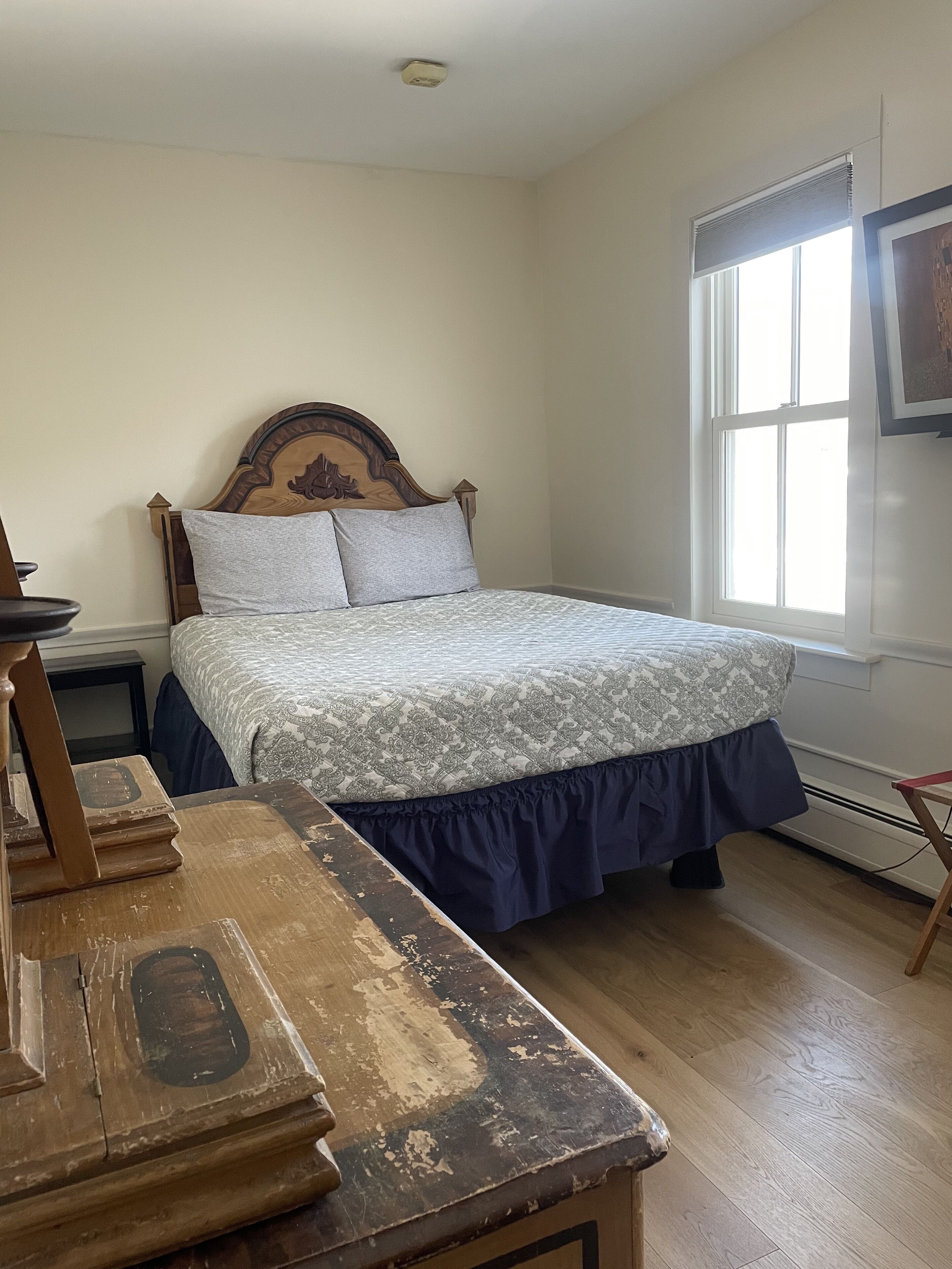 A bedroom with a wooden bed, a nightstand, a dresser, and a window with blinds.