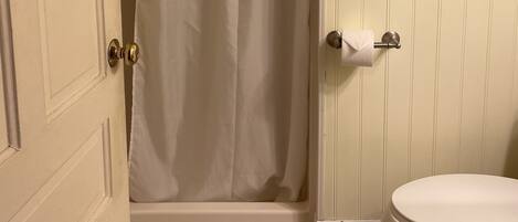 A bathroom with a shower, toilet, and a door with a towel hanging on it.