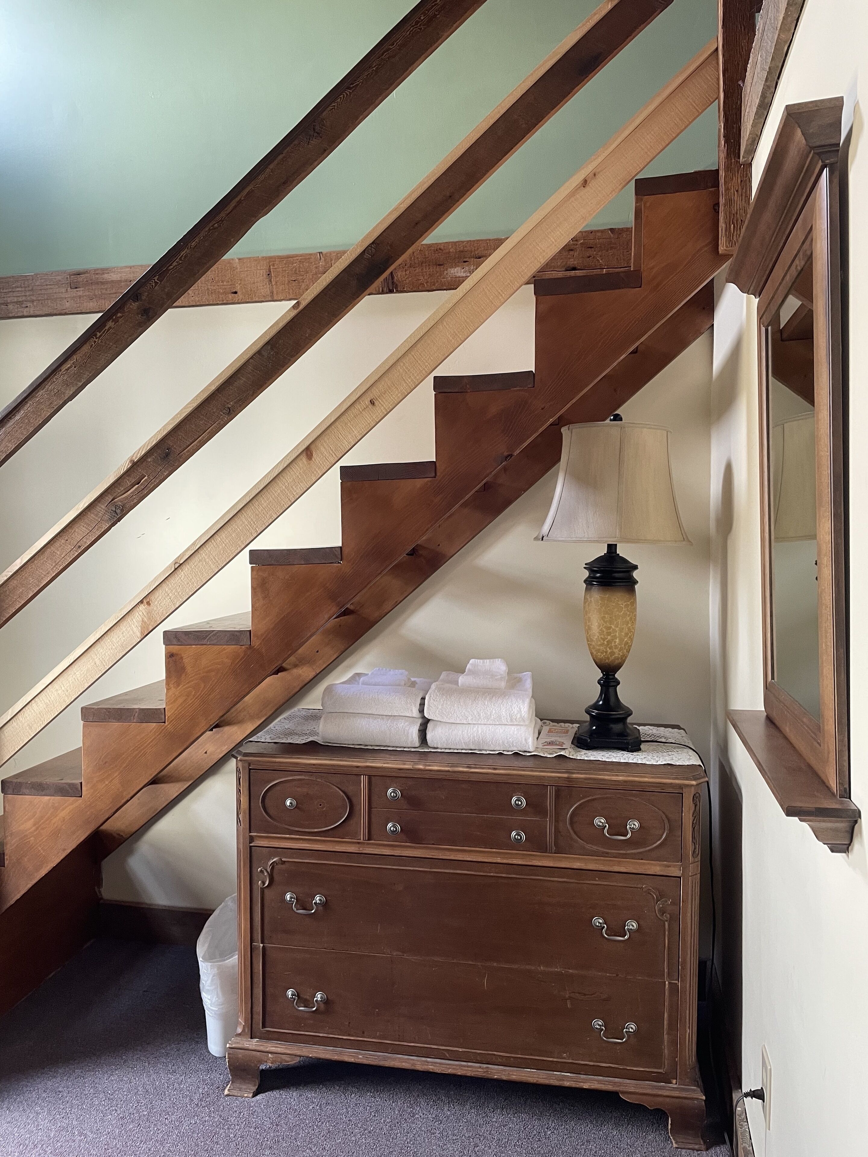 A wooden staircase with a lamp and folded towels on a dresser.