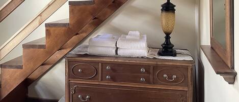 A wooden staircase with a lamp and folded towels on a dresser.