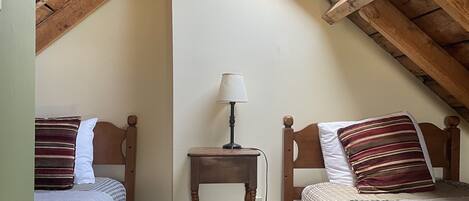 A small, cozy attic bedroom with two wooden beds, a nightstand, and a ceiling fan.