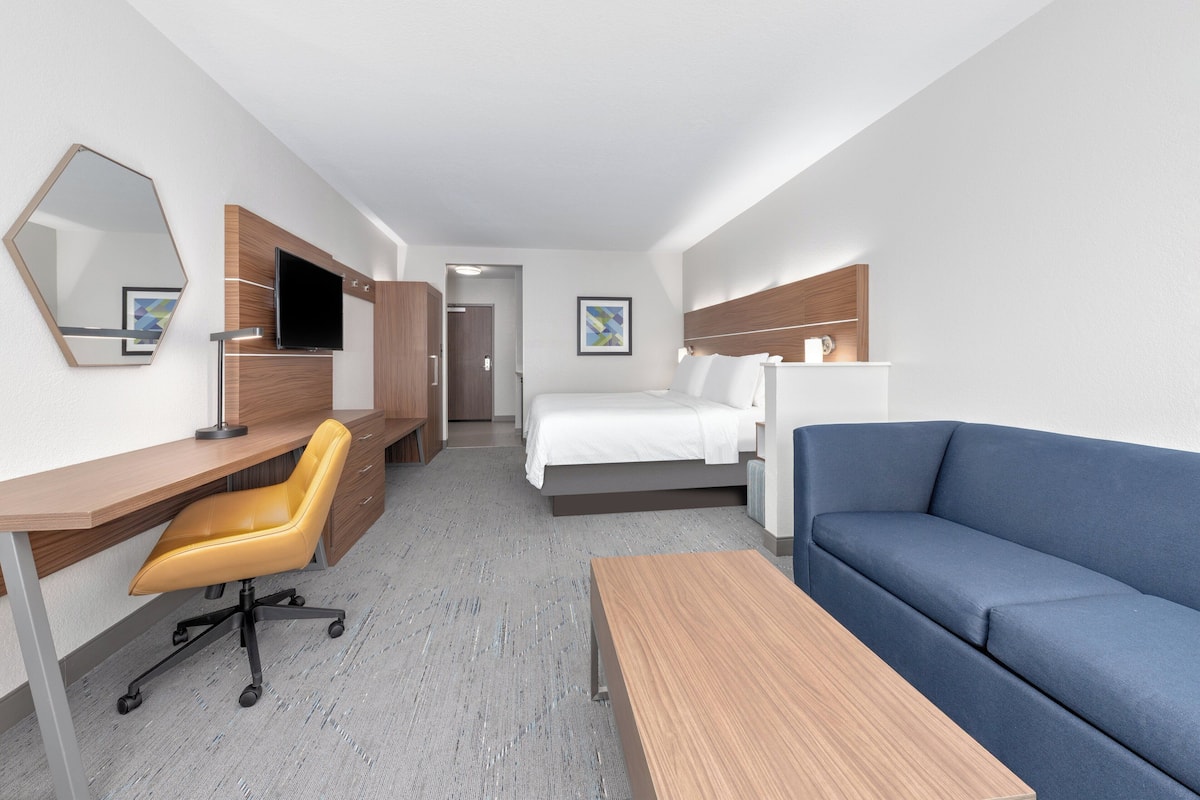 A hotel room with a desk, a blue sofa, a bed, and a TV.