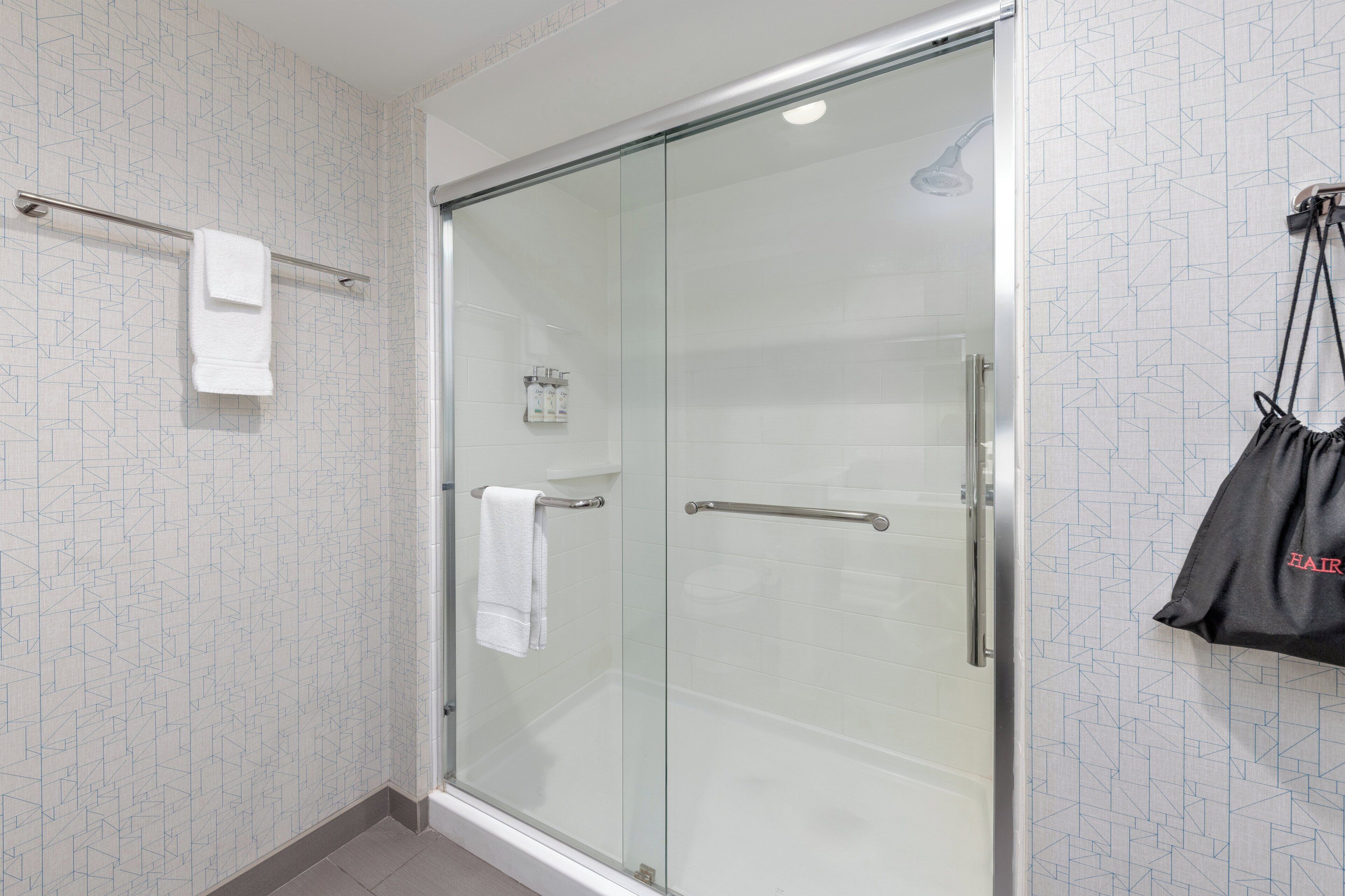 Un baño moderno con cabina de ducha de vidrio, un perchero y un bolso colgado de un gancho.