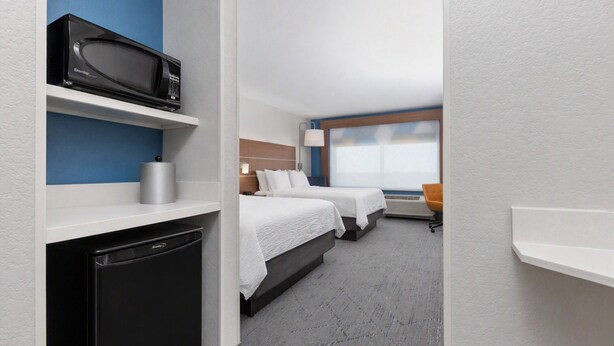 A hotel room with a bed, a desk, a microwave, and a chair.
