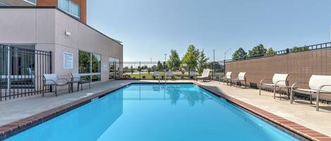 A swimming pool with lounge chairs and a building with a sign that reads "Pool Rules".