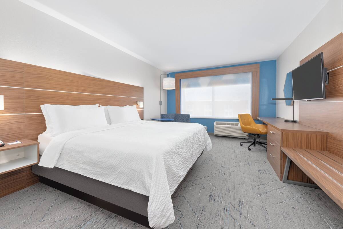 A modern hotel room with a large bed, a desk, a chair, and a TV.