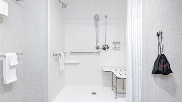 A modern shower area with a glass door, a handrail, and a small bench.