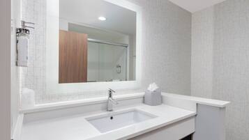 A modern bathroom with a large mirror, white sink, and a wooden vanity.