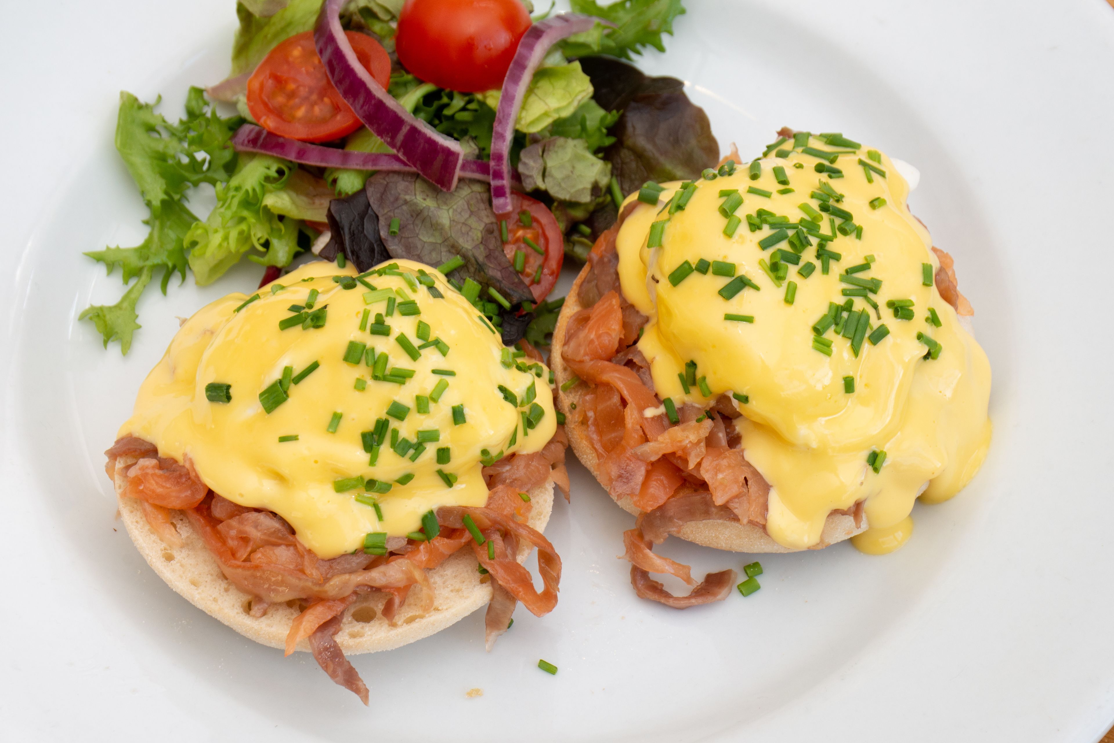 Un plato con huevos benedictinos y una ensalada acompañante.