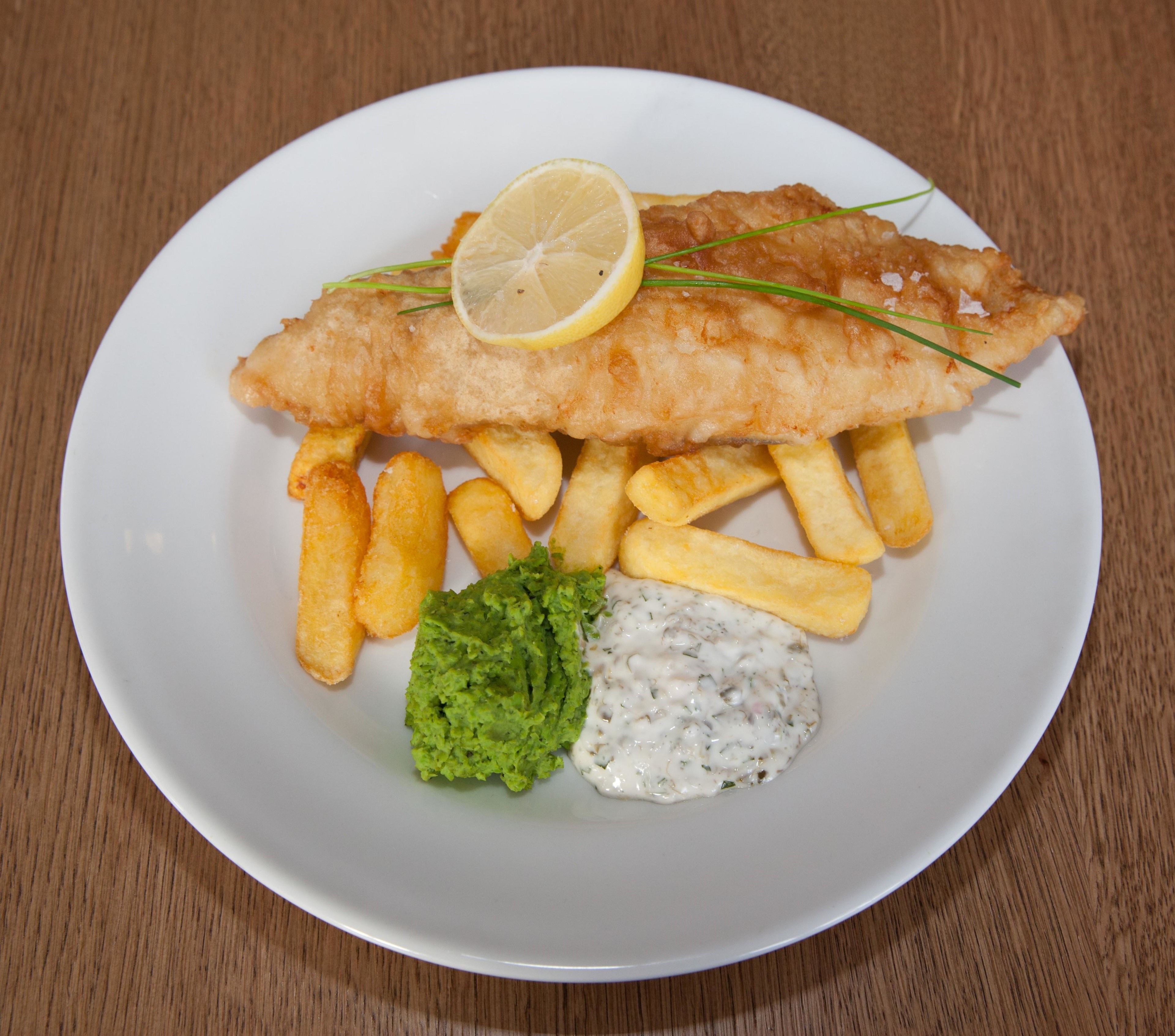 A plate with fish and chips, a slice of lemon, and two side dishes.