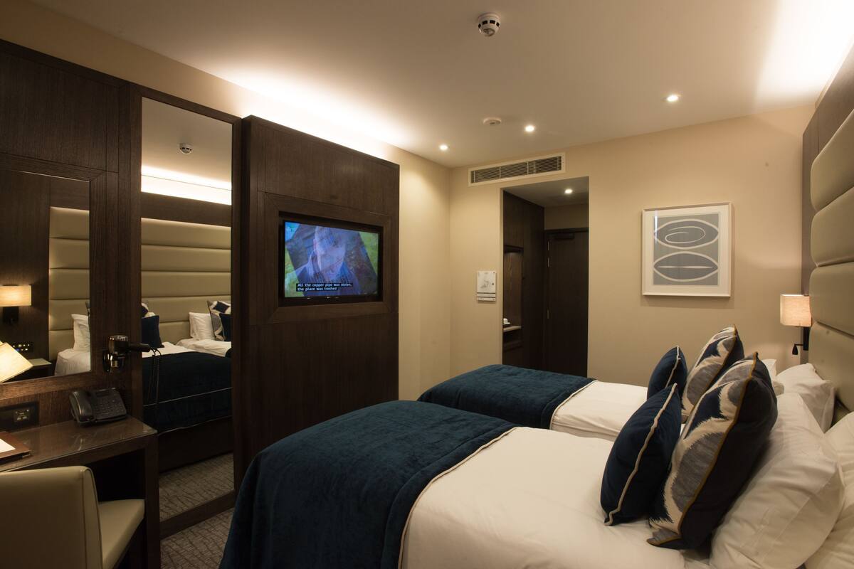 A hotel room with a bed, a desk with a phone, a TV, and a door leading to another room.