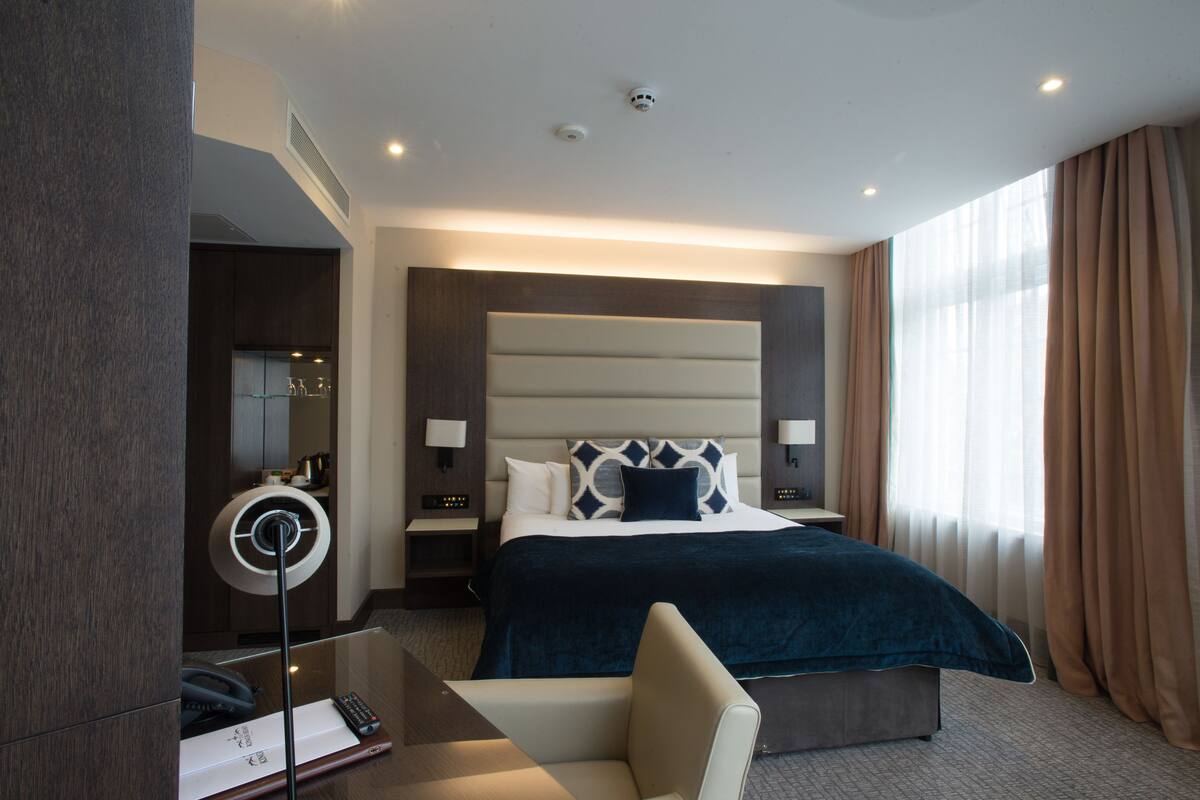 A modern hotel room with a large bed, bedside lamps, a desk with a telephone, and a mirror.
