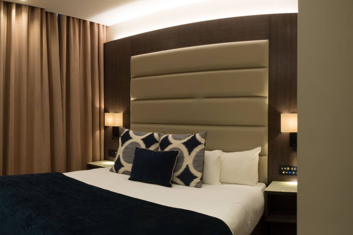 A hotel room with a large bed, a chair, a desk, and a curtain.