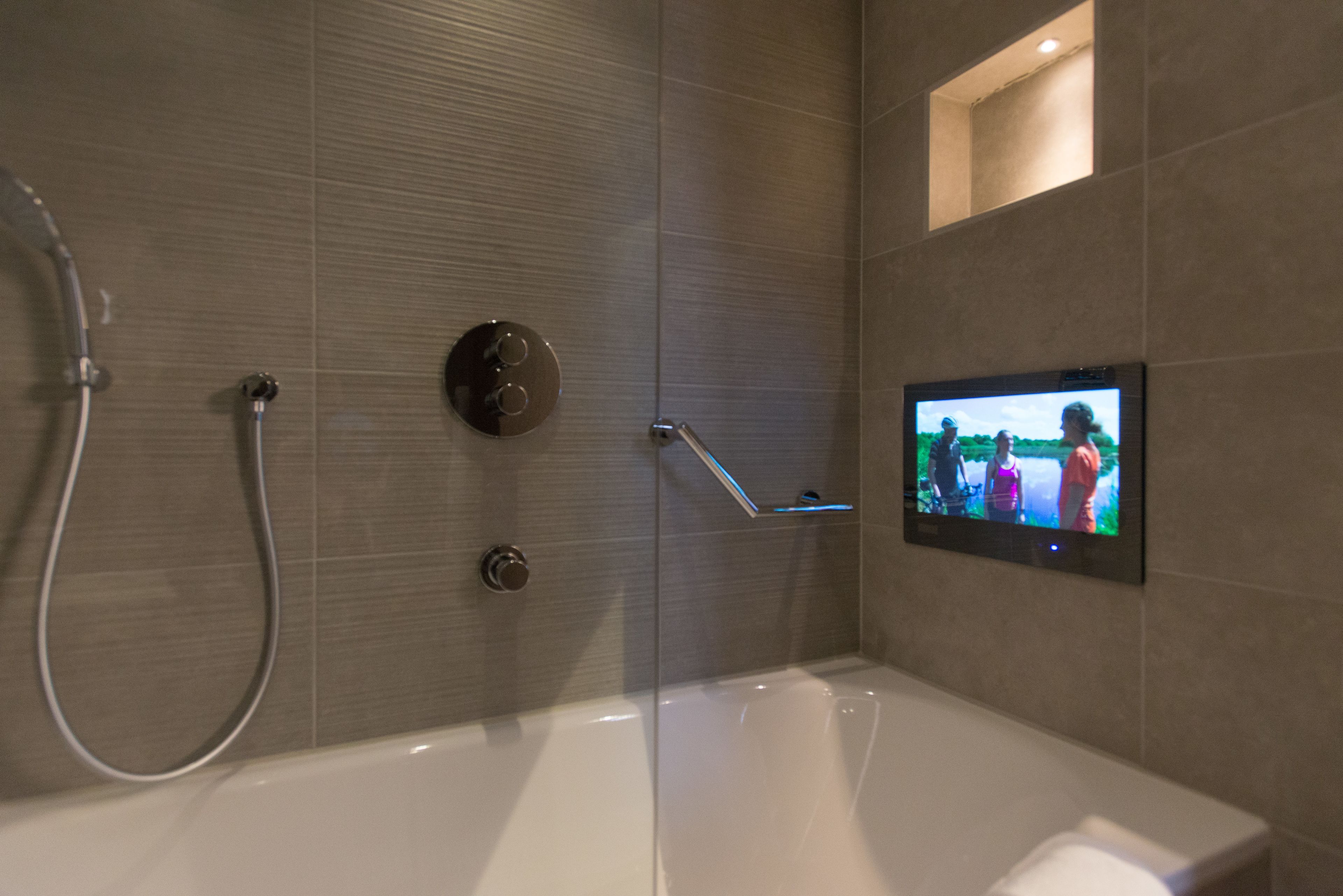 A modern bathroom with a bathtub, a handheld showerhead, and a wall-mounted TV.