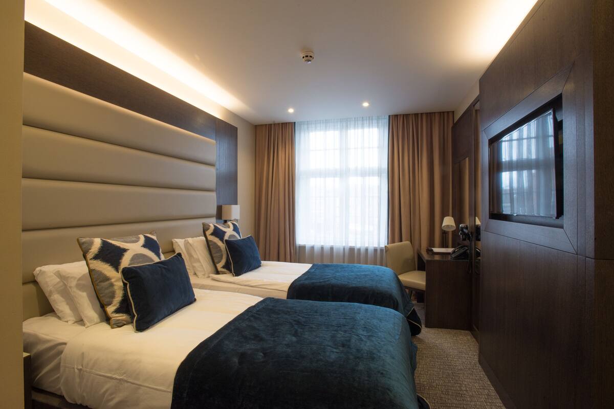 A hotel room with two beds, a desk, and a large window with curtains.