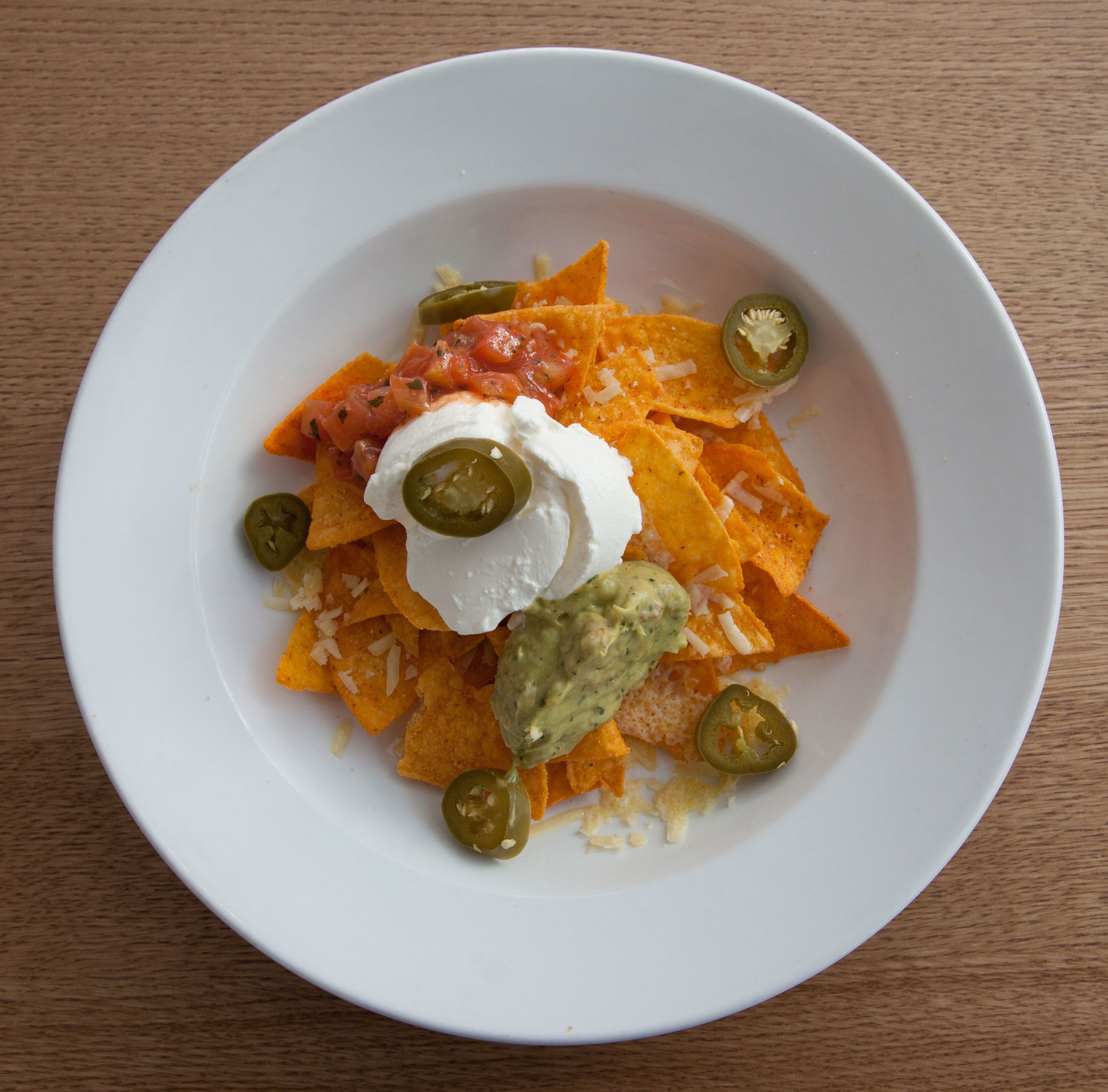 Lautasellinen nachoja, jonka päällä on smetanaa, guacamolea ja jalapeñoja.