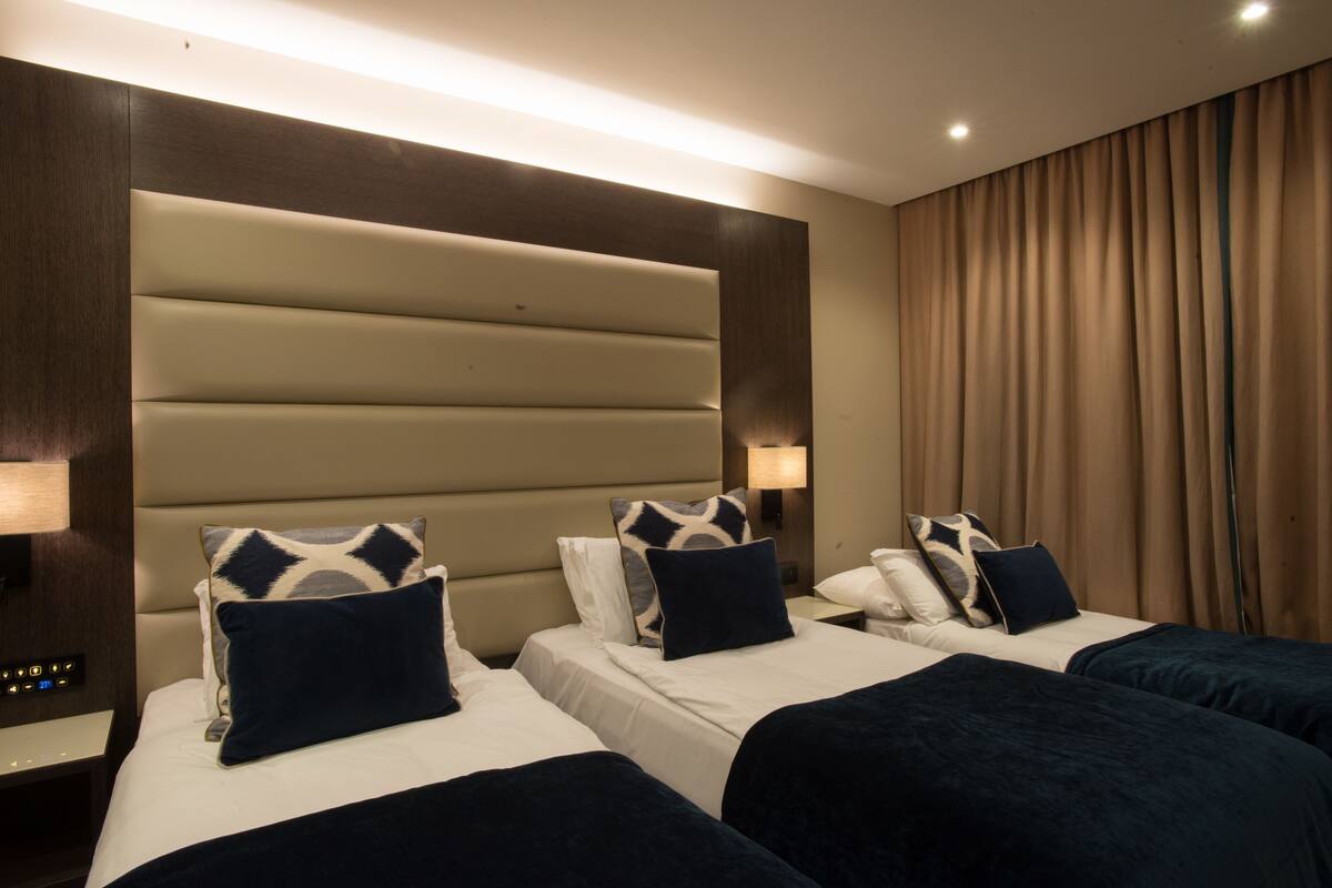 A hotel room with two beds, a large padded headboard, and a curtain on the window.