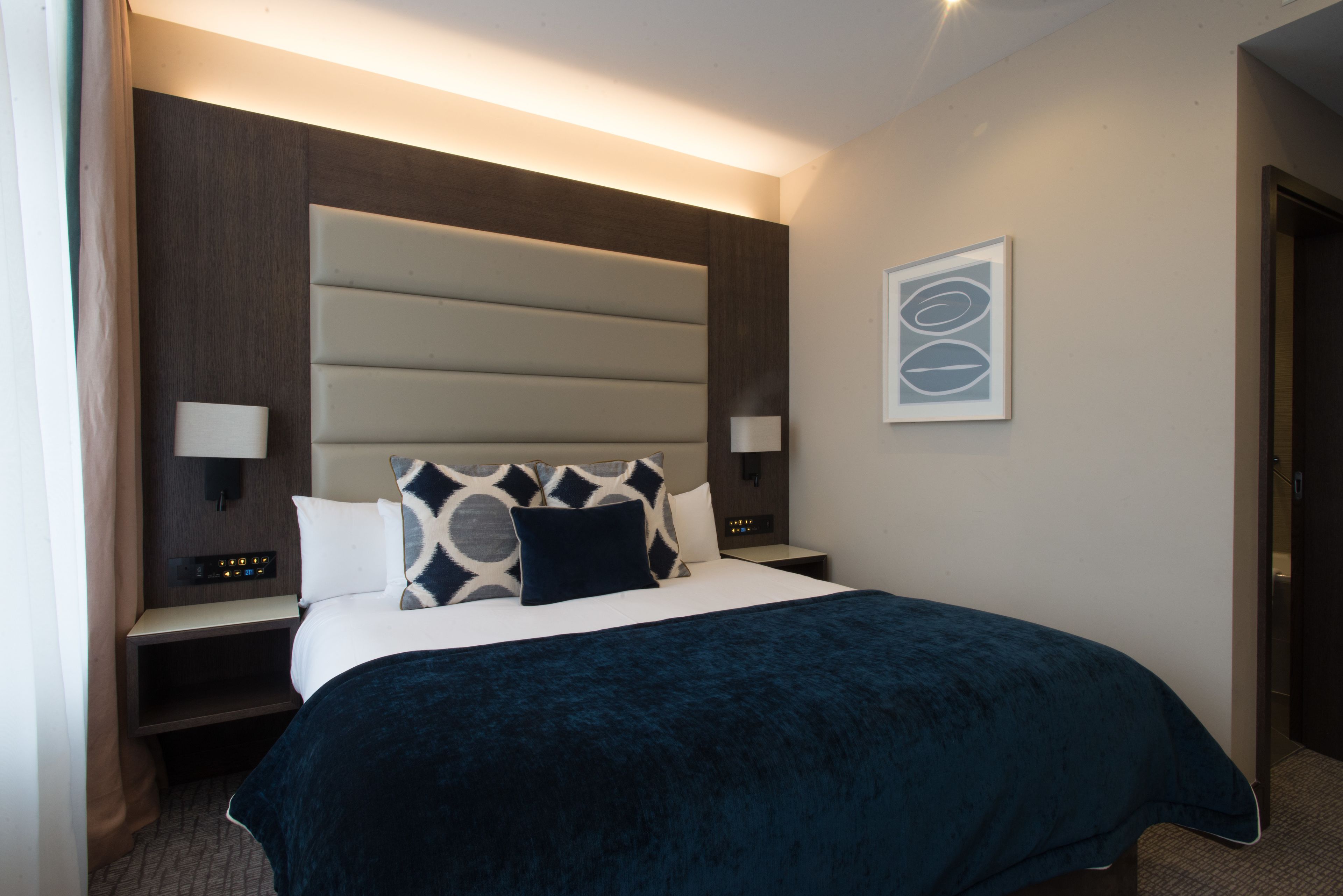 Een moderne hotelkamer met een groot bed, twee nachtkastjes, een bijzettafeltje en een wandlamp.