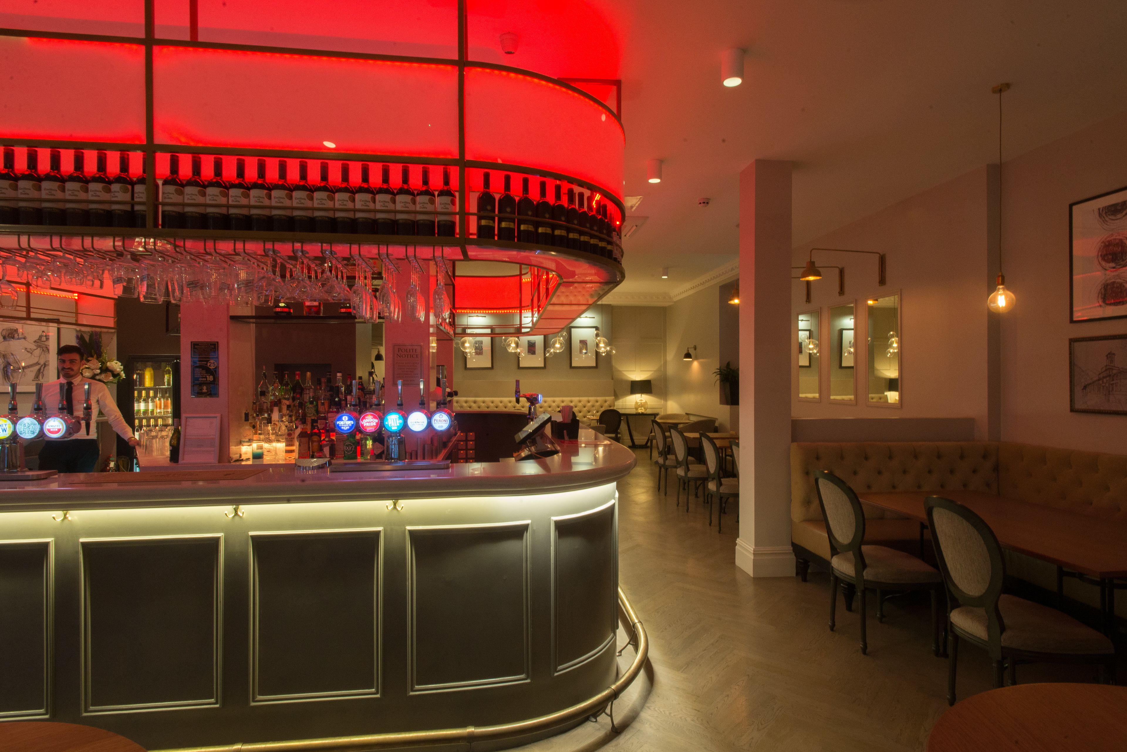 A bar area with a curved counter, multiple wine bottles, and a seating area with tables and chairs.