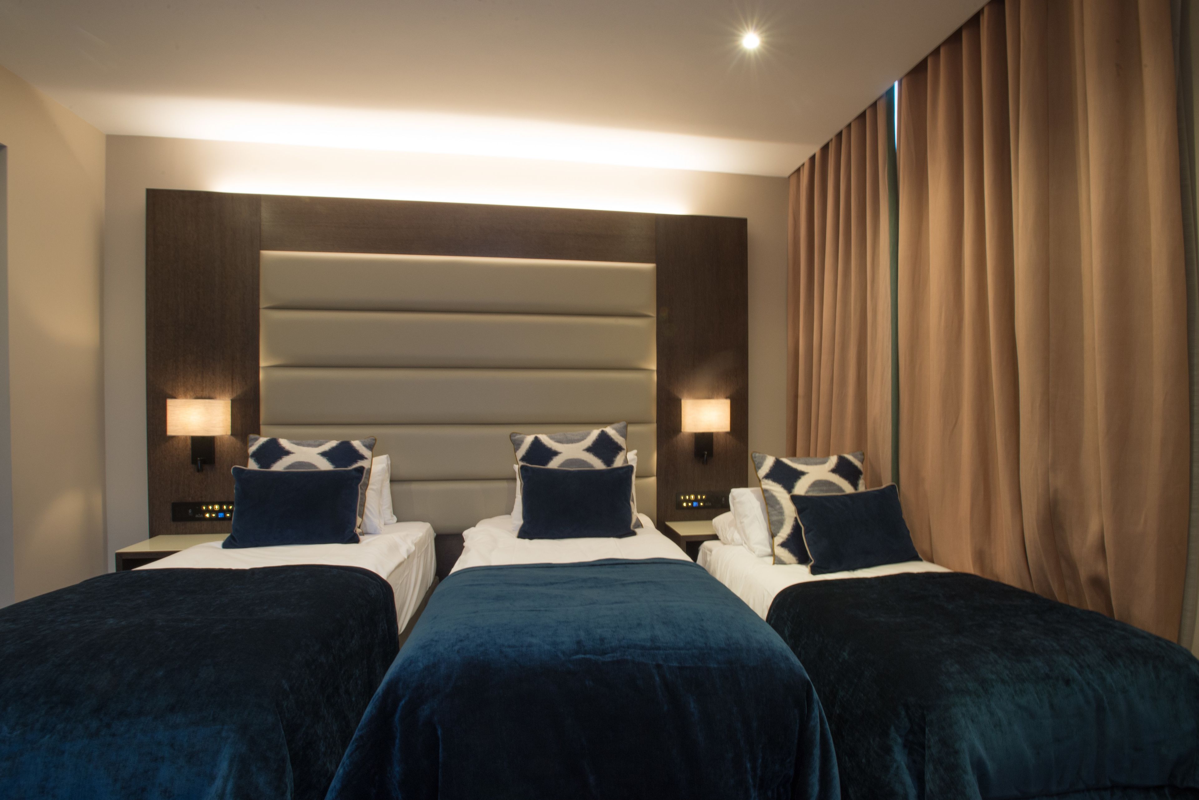 Une chambre d’hôtel avec deux lits, chacun doté d’une tête de lit, de lampes de chevet et d’une literie bleu foncé.
