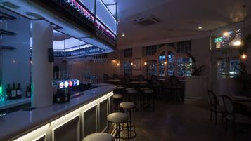Una zona de bar con mostrador, taburetes y estanterías llenas de botellas.