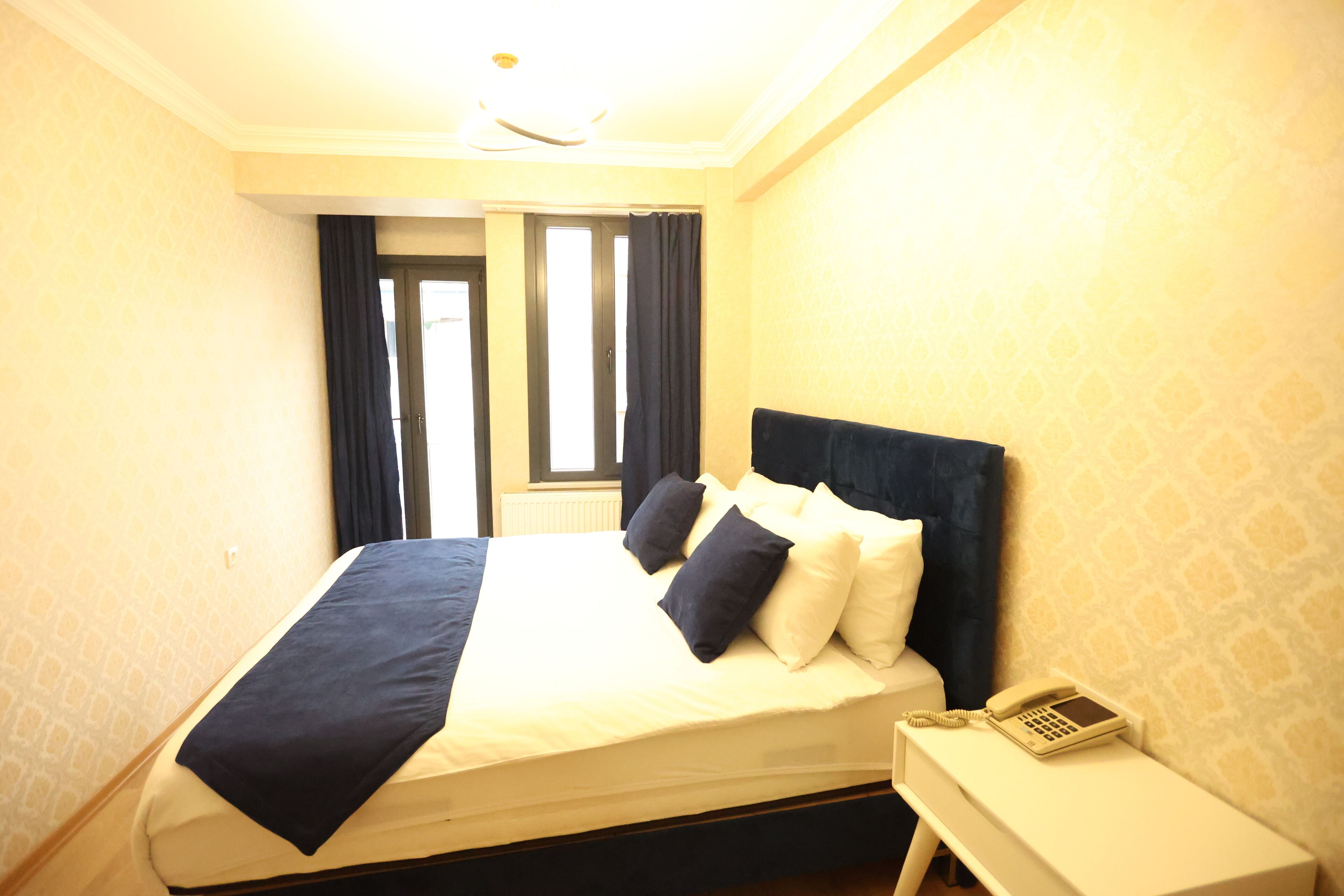 A hotel room with a bed, a bedside telephone, and a window with curtains.