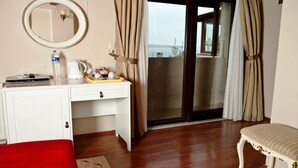 Ett hotellrum med trägolv, ett vitt skrivbord med en spegel, en röd bänk och utsikt genom en glasdörr.