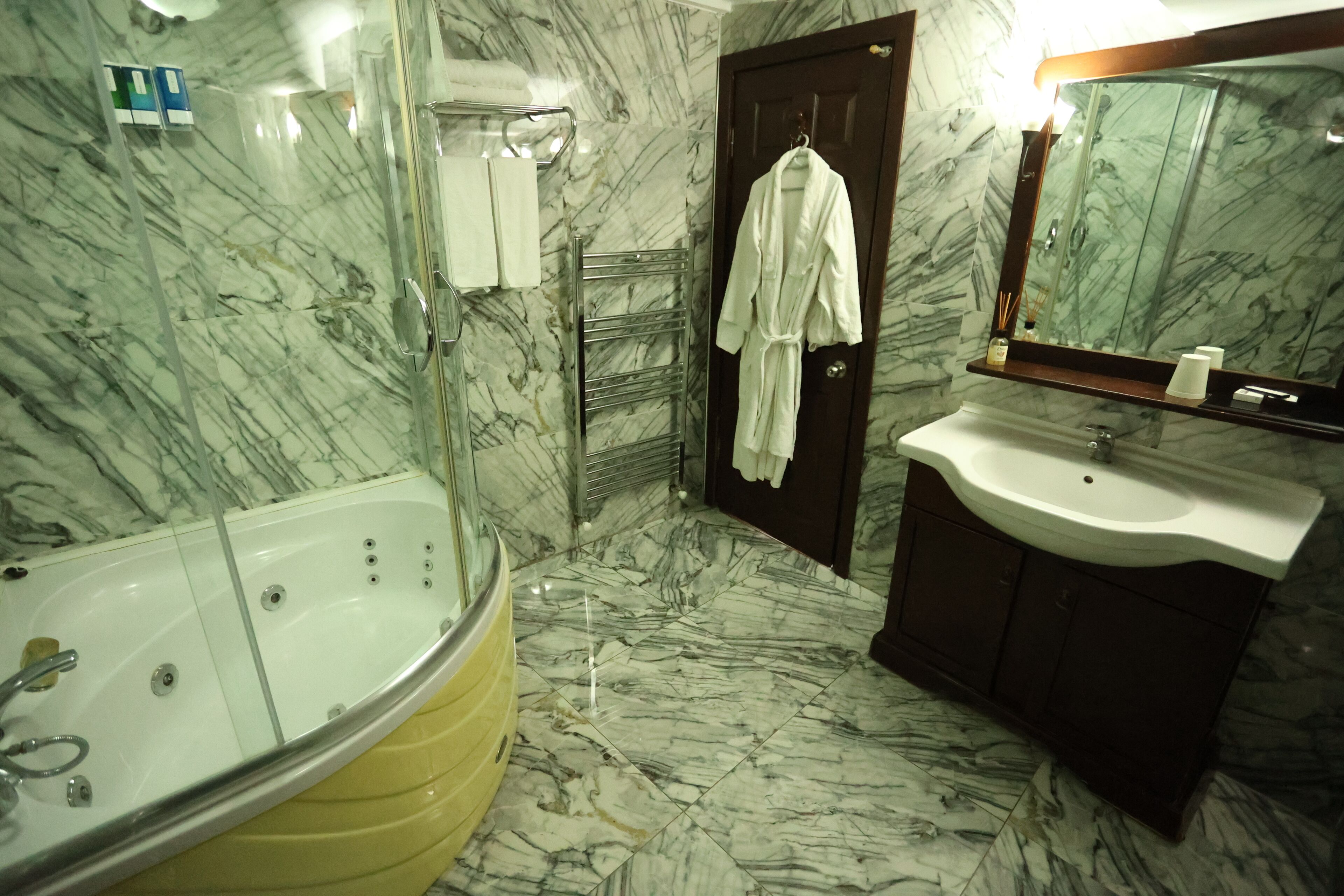 Un baño con piso de mármol, una bañera, un lavamanos y un espejo.