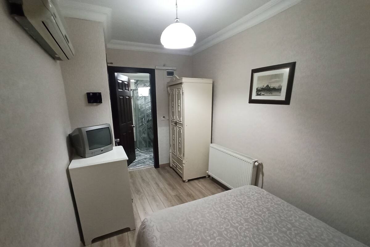 A small, neatly arranged bedroom with a bed, a television, a wardrobe, and a radiator.