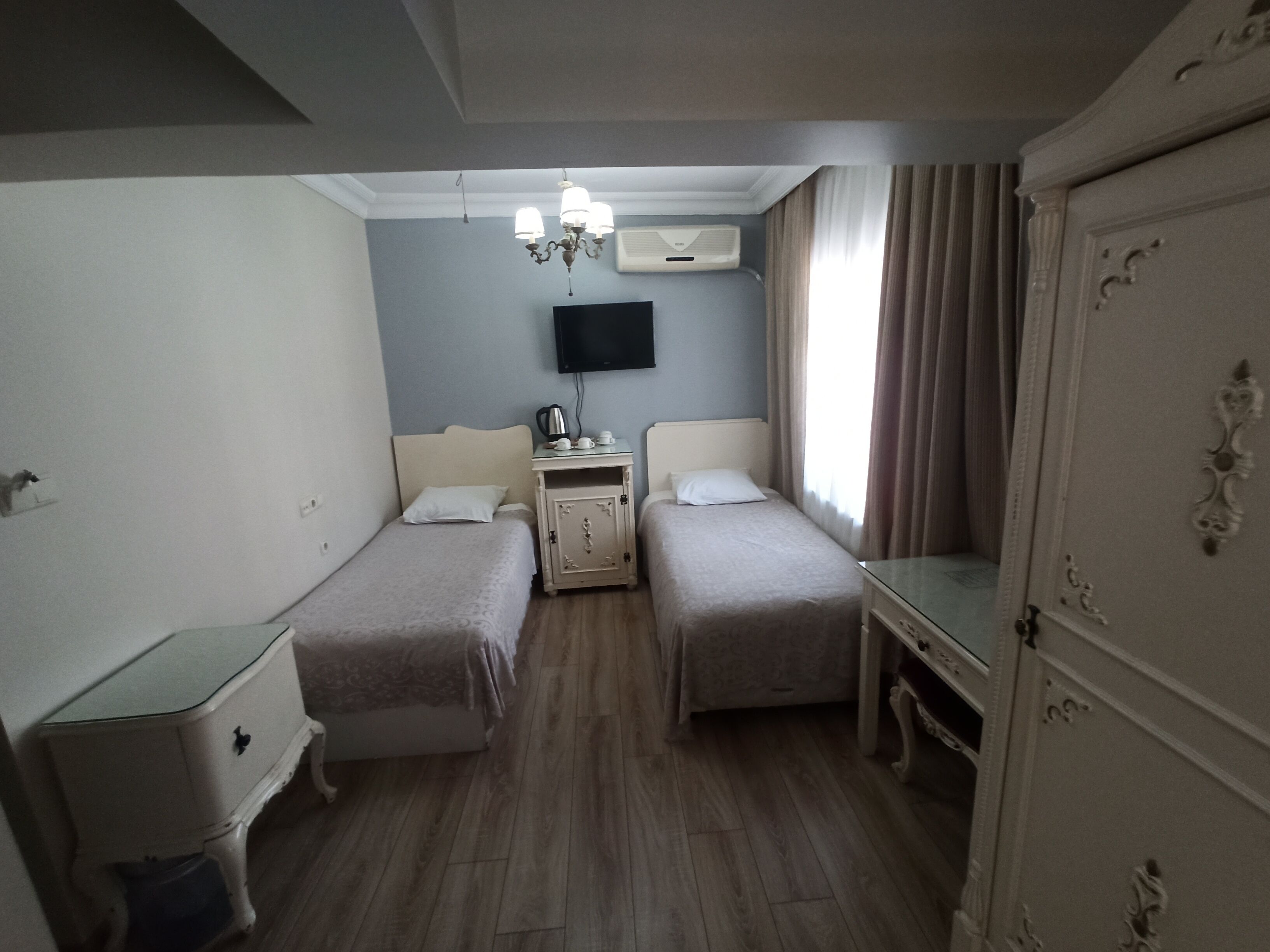 Habitació d'hotel amb dos llits, televisió, armari i una taula petita amb una papereta i tasses.