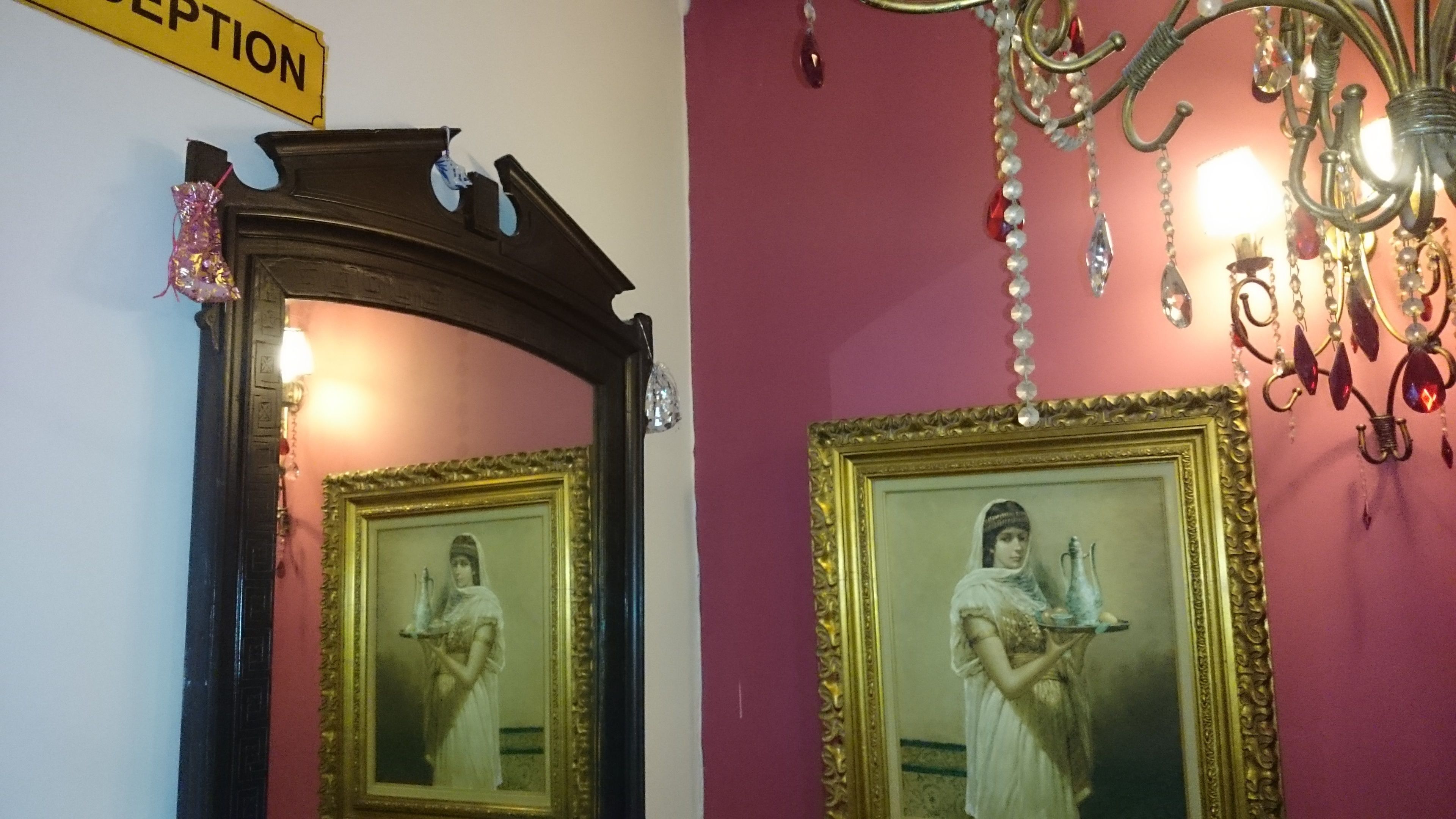 Quarto com um espelho refletindo uma pessoa, um candelabro e uma placa acima do espelho.